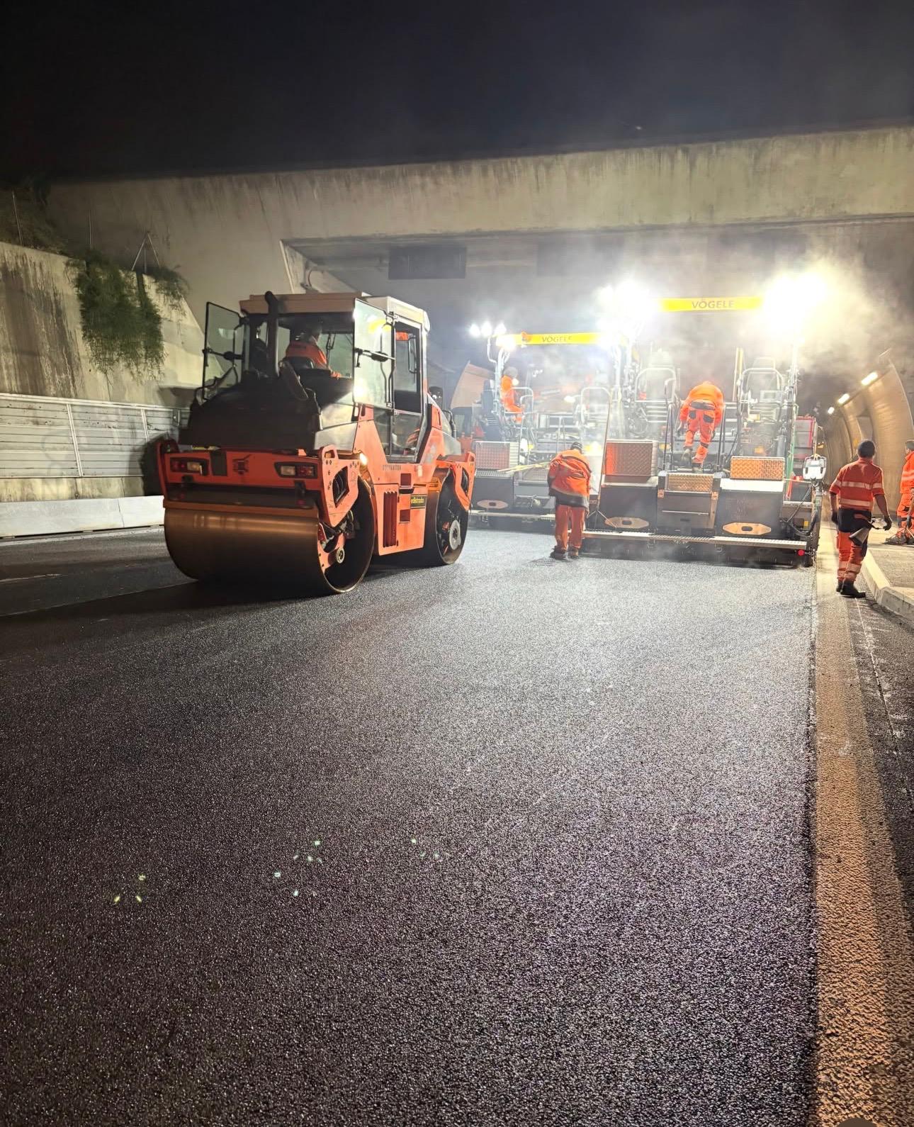Equipe executando pavimentação asfáltica em túnel durante operação noturna